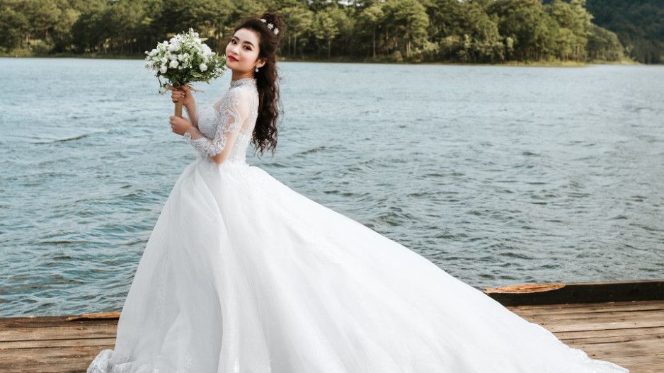 Asiatische frau in weißem Brautkleid mit langer Schleppe am See