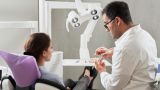 Zahnarzt mit Patientin in Zahnarztordination erklärt Behandlung